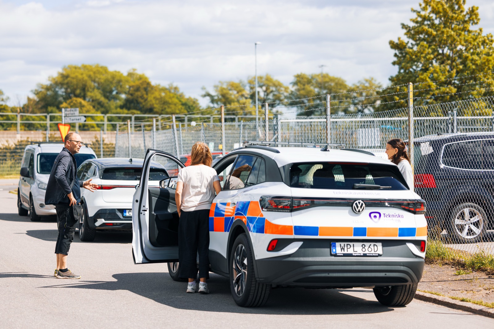 Nyfolierad elbil med Tekniska verkens profil, tre personer samtalar vid bilen