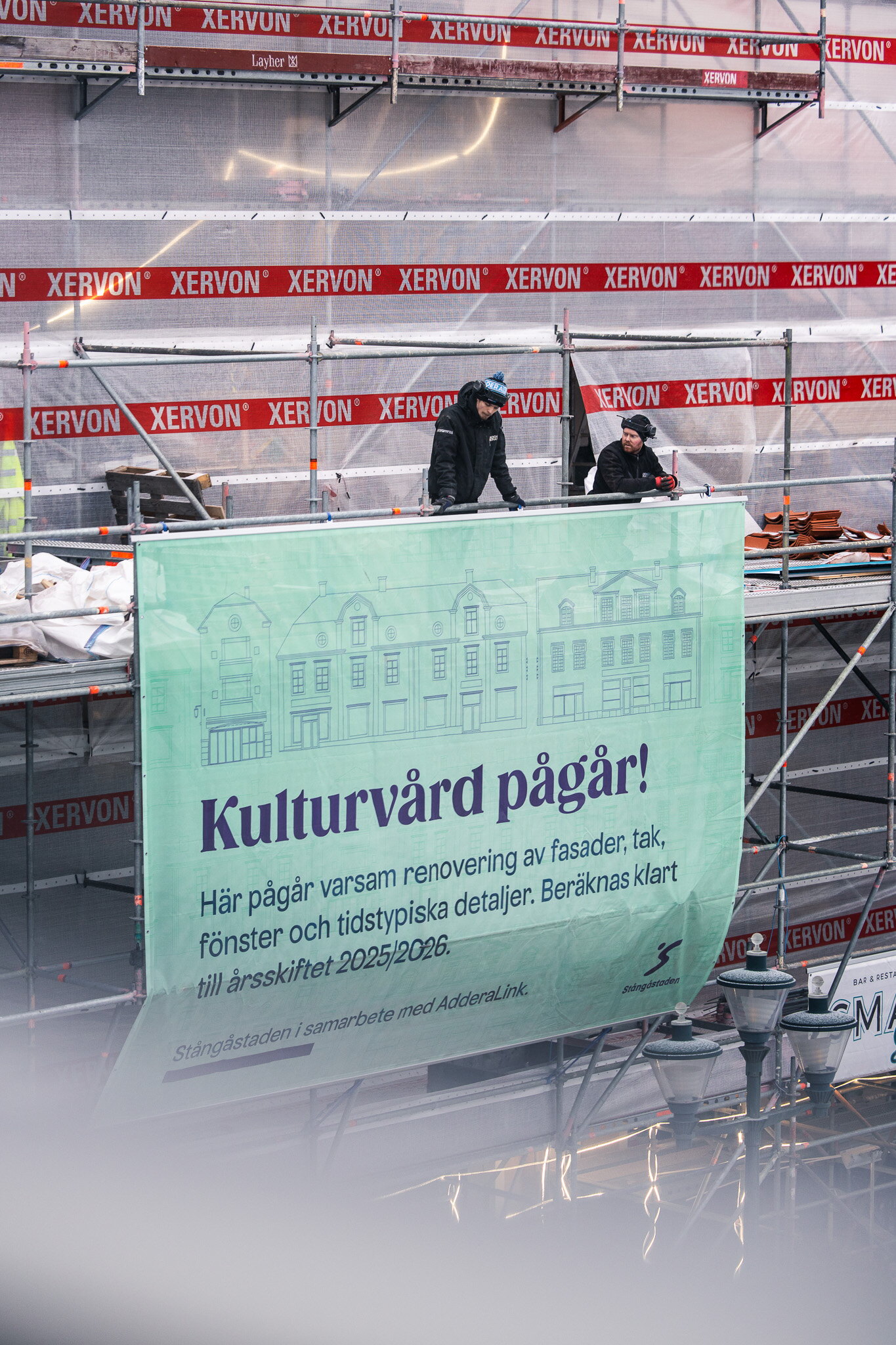 Montörer fäster en stor informationsvepa på byggställning under en fasadrenovering