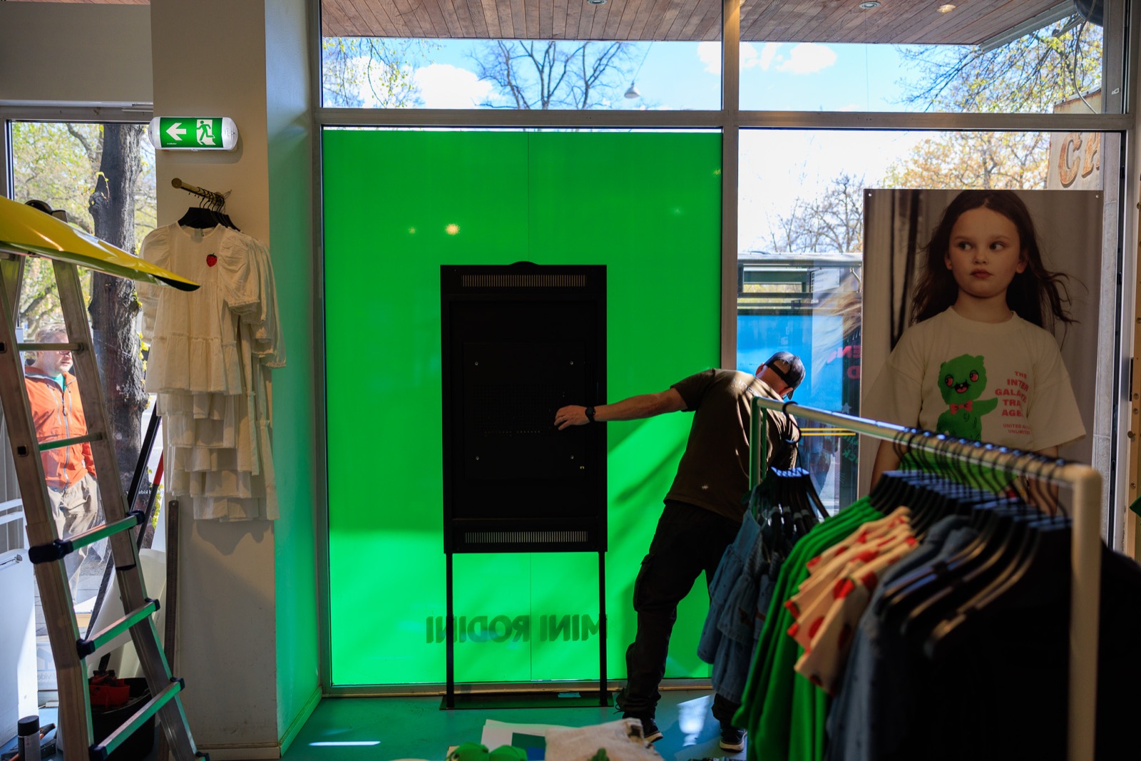 Montör installerar en digital skärm framför ett grönt folierat skyltfönster i en klädbutik