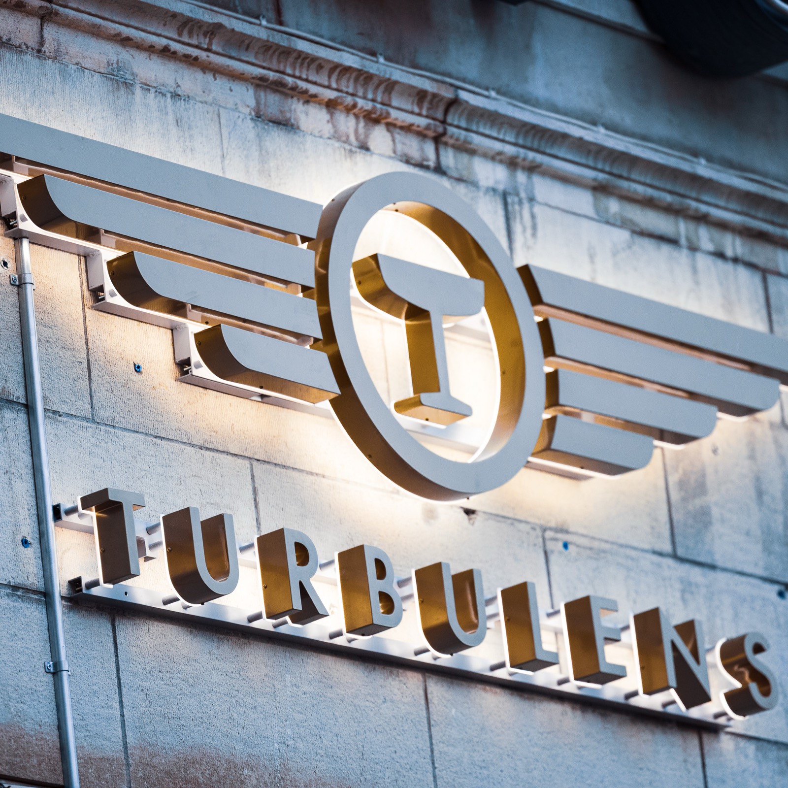 Närbild på Turbulens fasadskylt med vingformad logotyp och friskurna bokstäver med bakbelysning