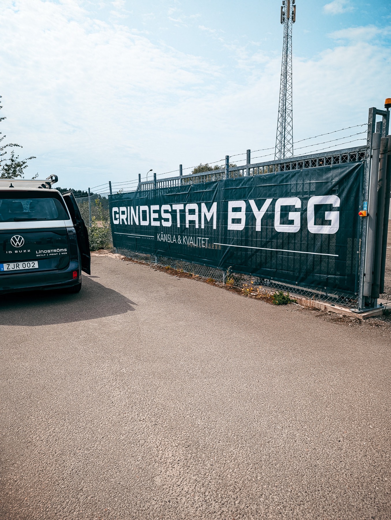 Lång mörk vepa med texten Grindestam Bygg uppspänd på en grind utomhus