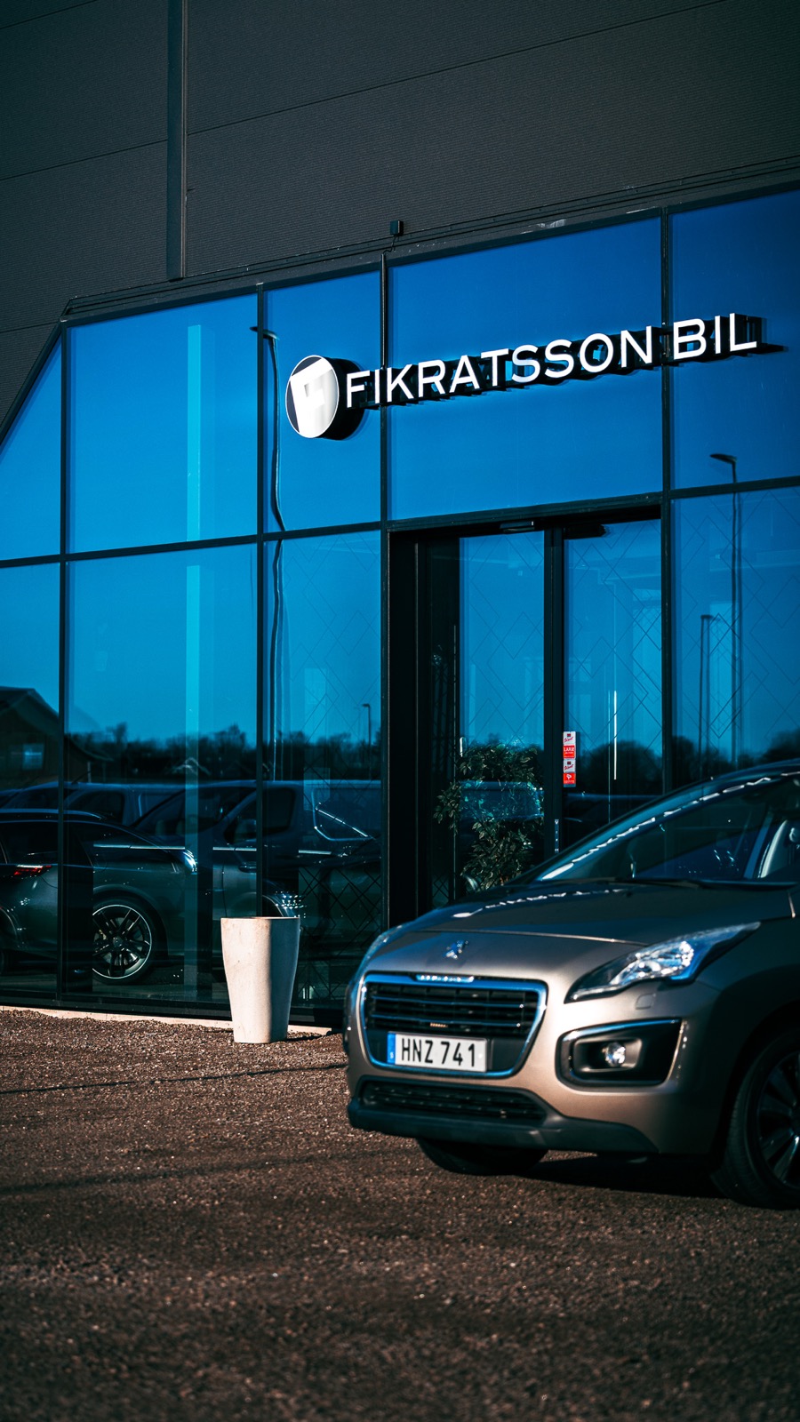 Fikratsson Bils entré i kvällsljus med belyst logotypskylt och friskurna bokstäver över glasfasaden