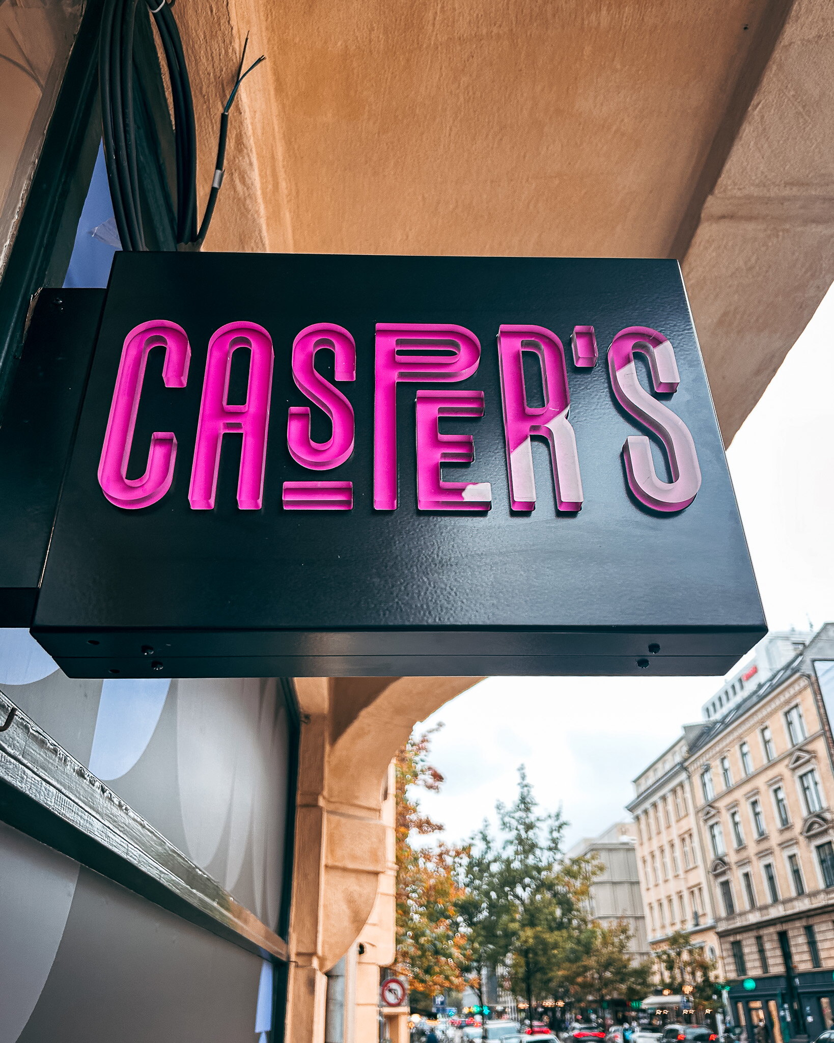 Svart utstickande skylt med rosa belysta Casper's-bokstäver på restaurangfasad i Köpenhamn