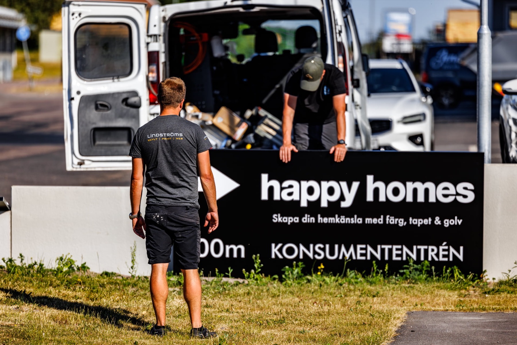 Två montörer monterar en hänvisningsskylt för Happy Homes, med servicebilen bakom