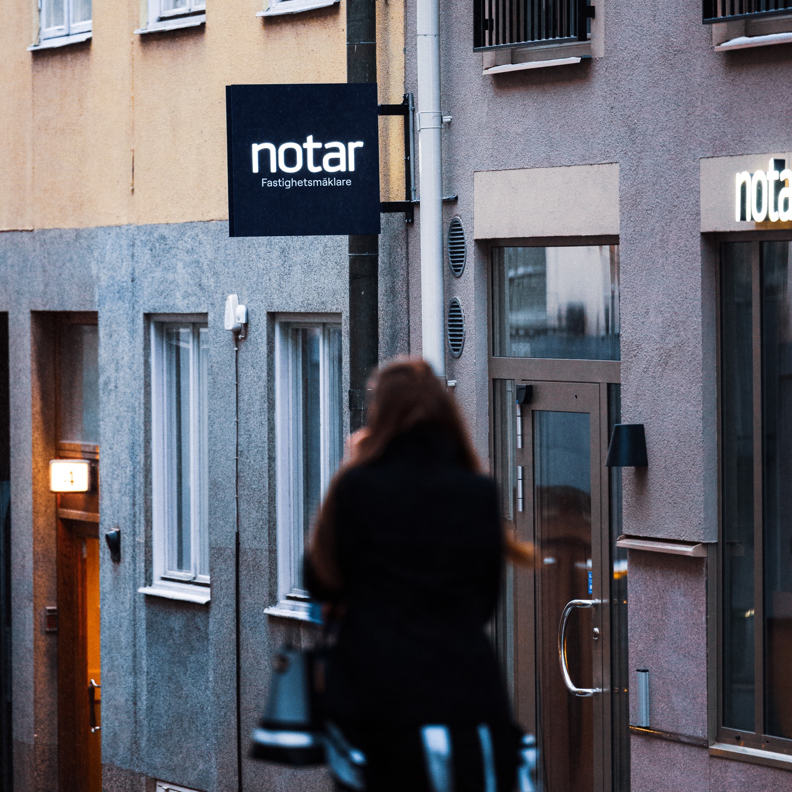 Notars mörkblå flaggskylt monterad på fasad i skymning