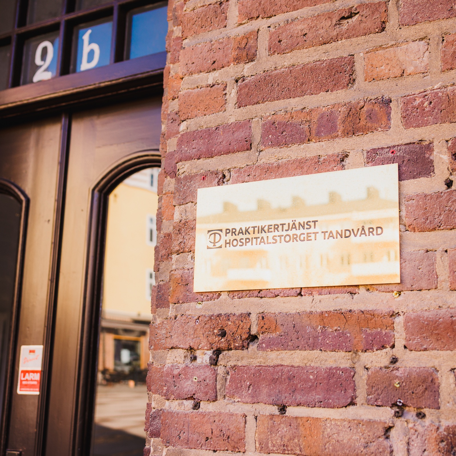 Metallskylt med Praktikertjänst Hospitalstorget Tandvård på tegelfasad