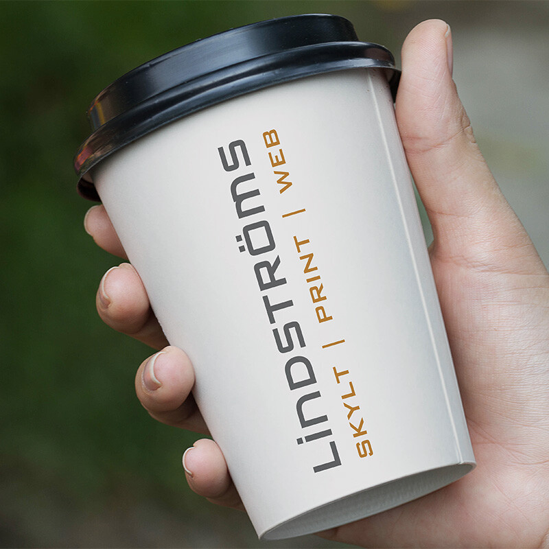 Pappersmugg med Lindströms logotyp i en hand utomhus