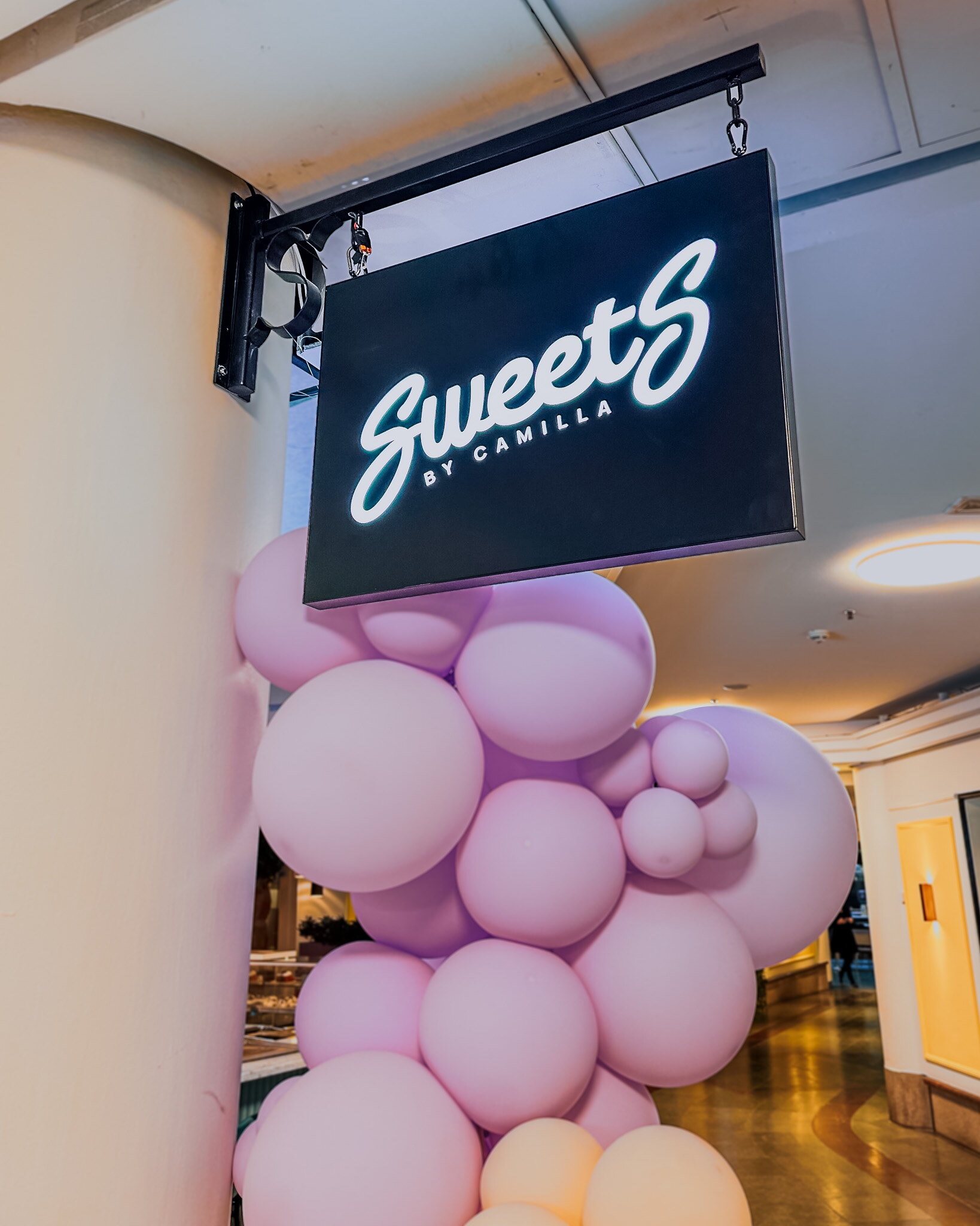 Utstickande svart ljusskylt med vit Sweet's-logotyp ovanför restaurangens entré