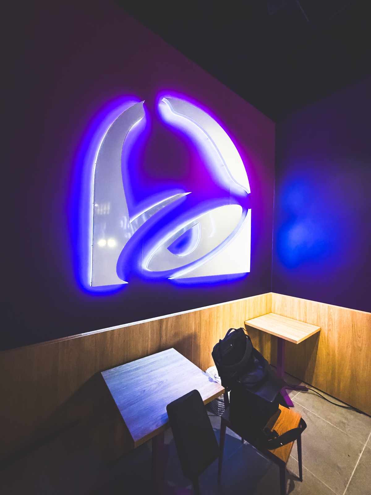 Taco Bells klocklogotyp som väggskylt med lila LED-kontur ovanför sittplatser