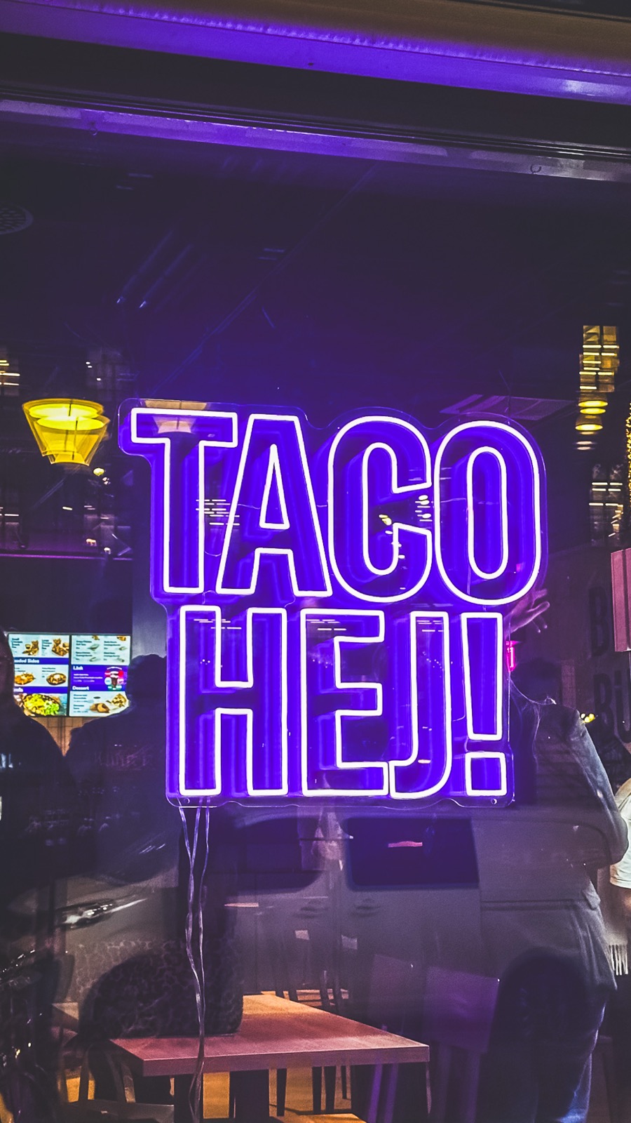 Neonskylt i skyltfönstret med texten TACO HEJ! i lila ljus