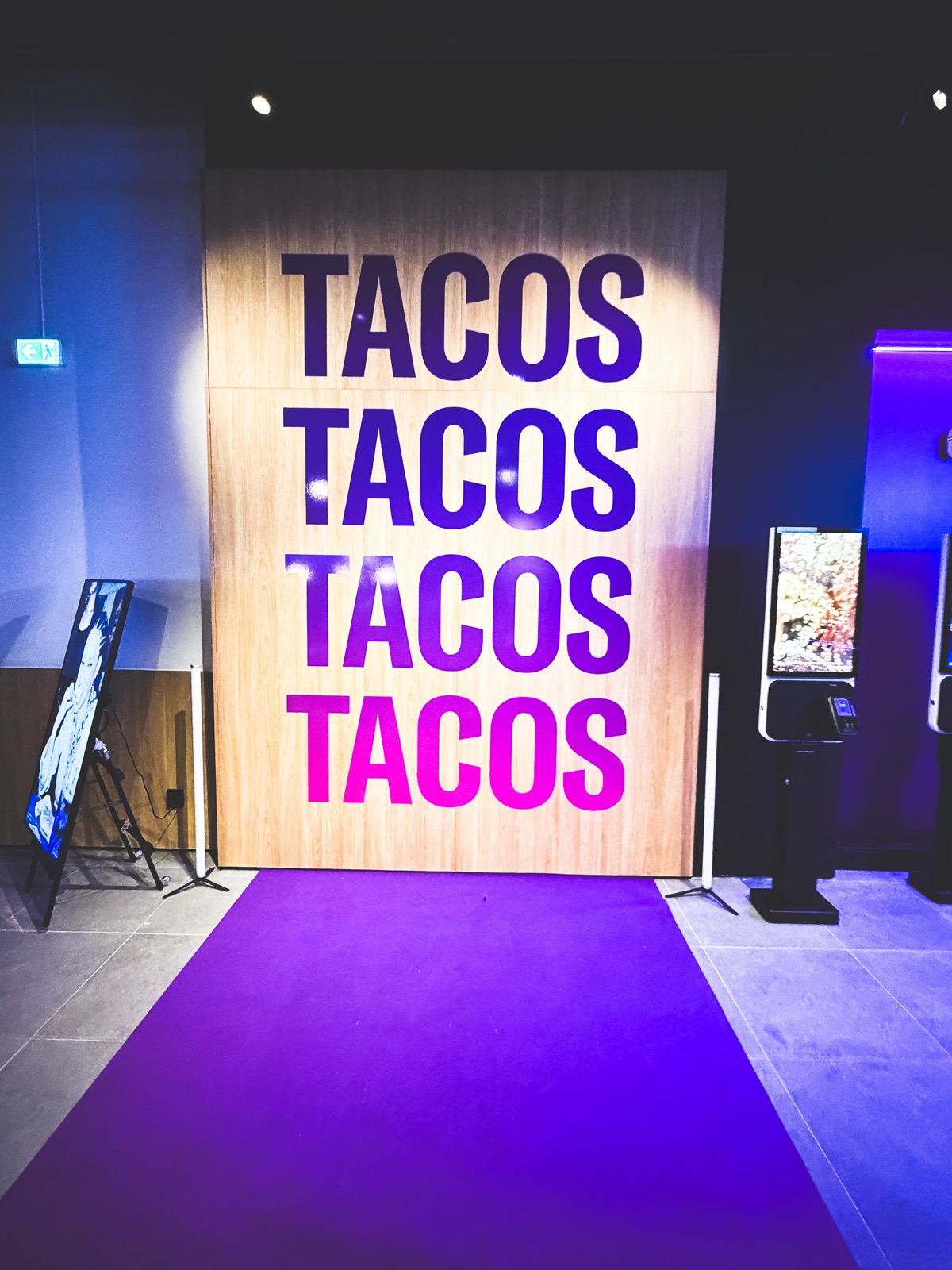 Väggpanel i trä med ordet TACOS folietryckt fyra gånger i toner från lila till rosa