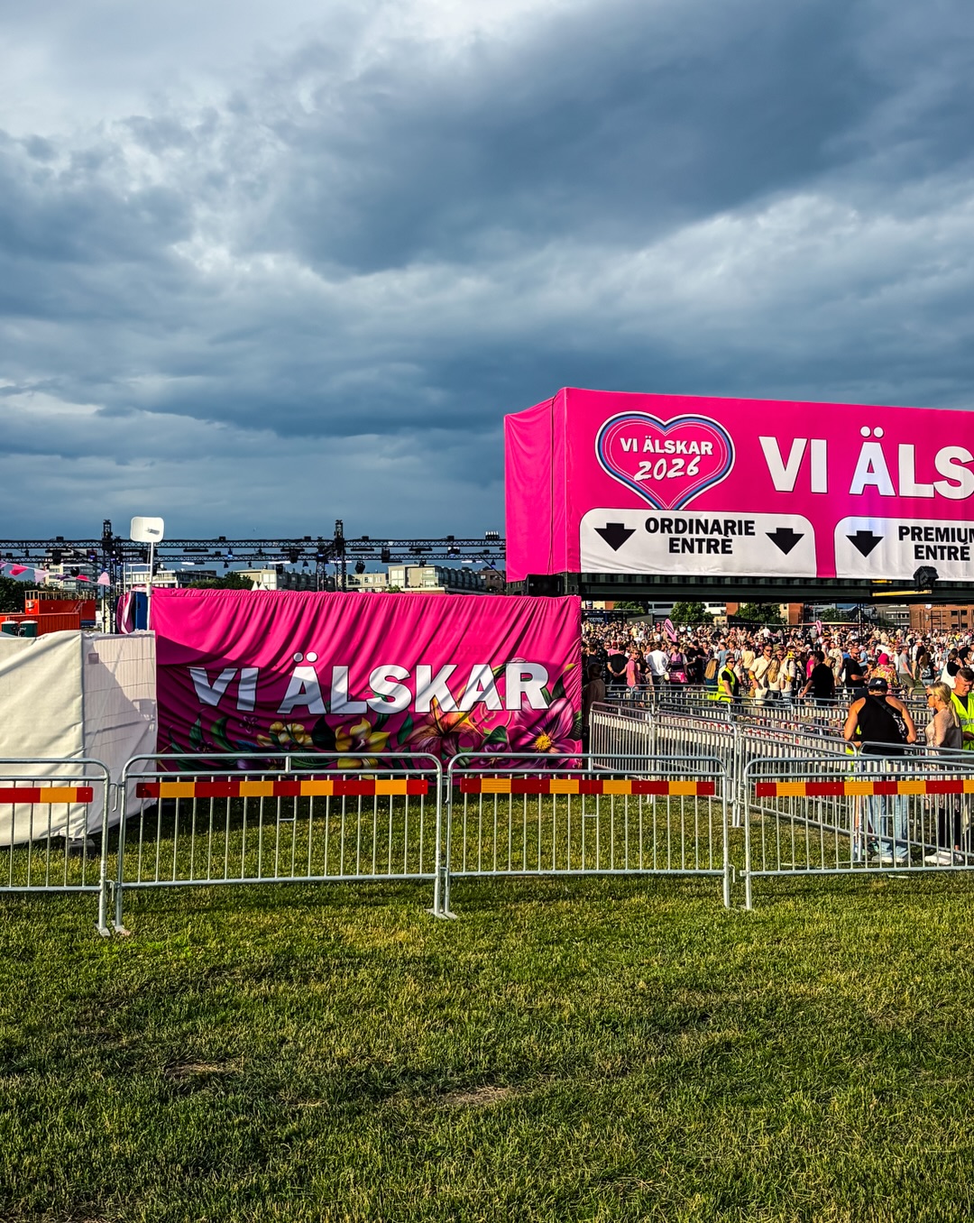 Rosa staketvepor med texten Vi Älskar längs kravallstaket framför entrén, folkmassa i bakgrunden under mulen himmel